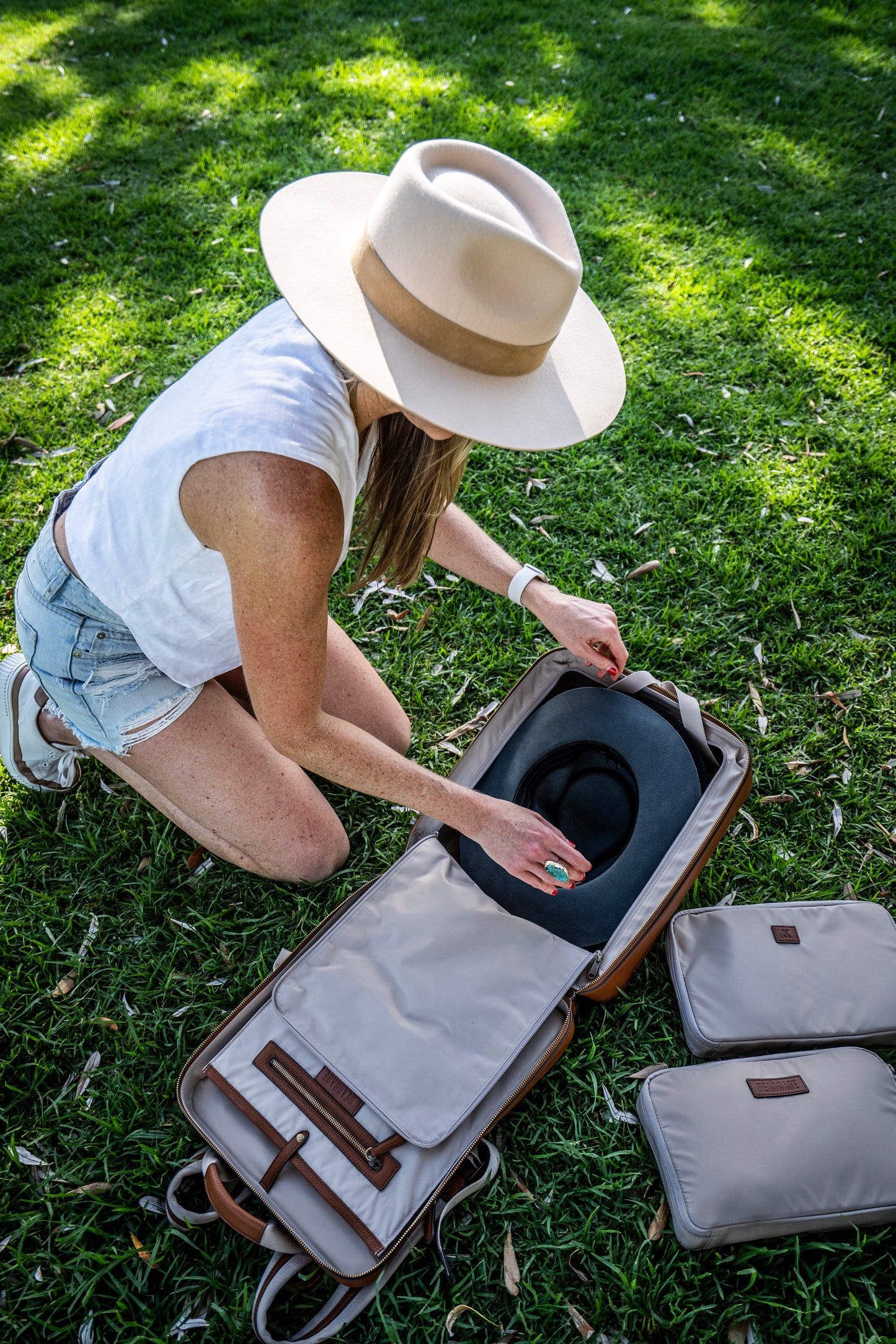 woman with hat packing a hat inside the headcase backpack bondi bombshell brown backpack with 2 packing cubes